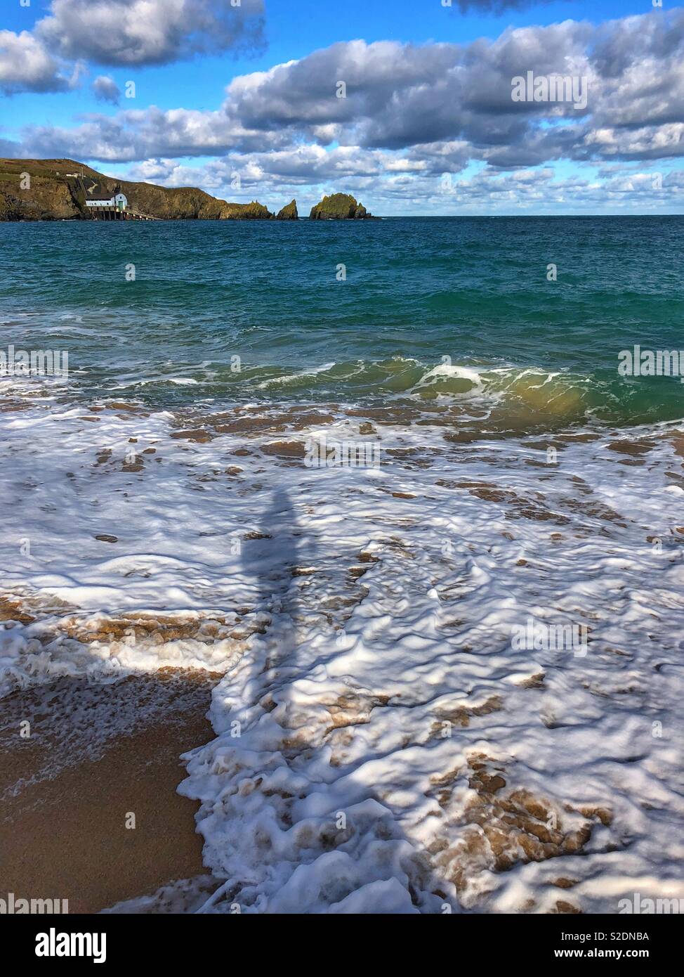 Shadow of an angler fishing on the North Cornwall coast, November. Padstow lifeboat station in the distance. Stock Photo