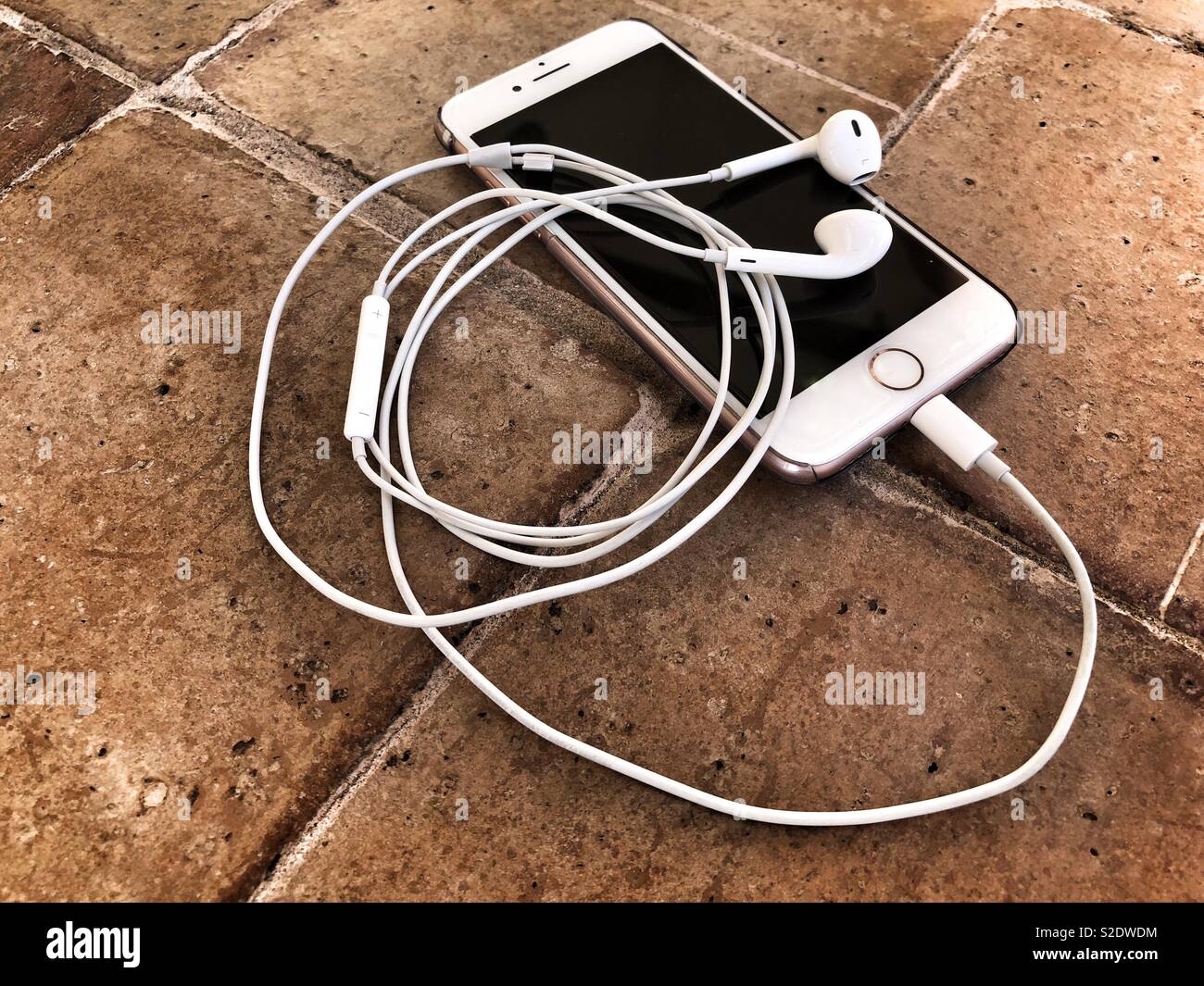 Smartphone and earphones on terracotta tiled floor - Smartphone Captured Stock Image