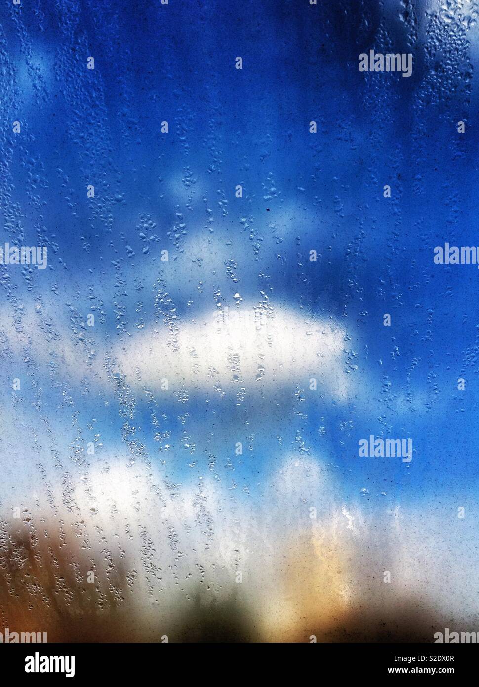 White clouds and blue sky seen through a dirty smudged window dripping with moisture - Smartphone Captured Stock Image