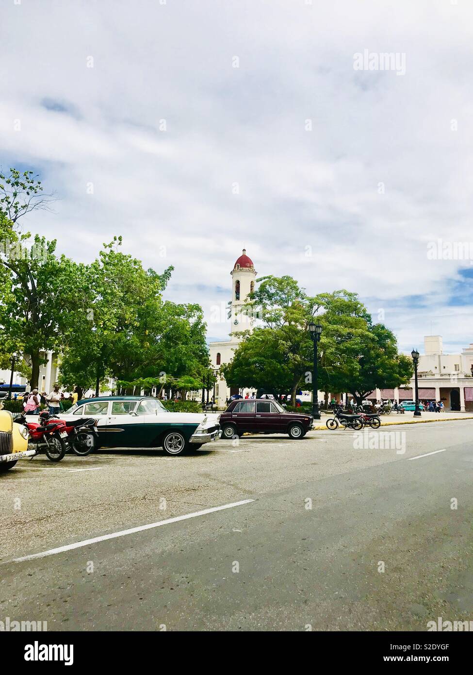 Classic cars and motorbikes parked along the road in the main square outside Jose Marti Park in Cienfuegos Cuba Stock Photo