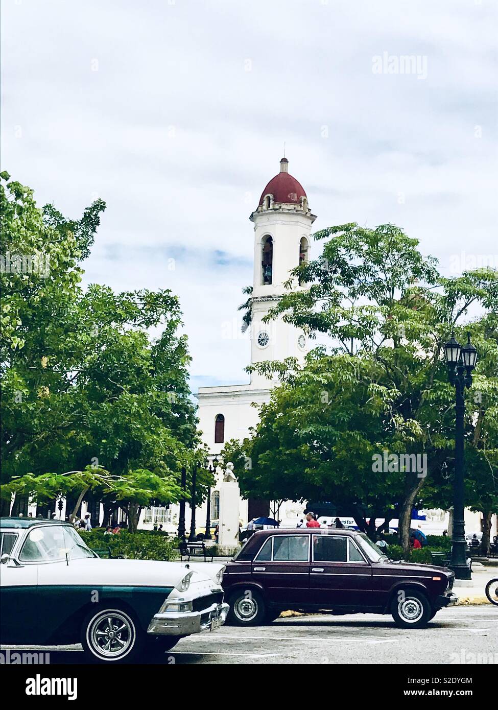 Classic cars driving past the cathedral in Cienfuegos Cuba Stock Photo