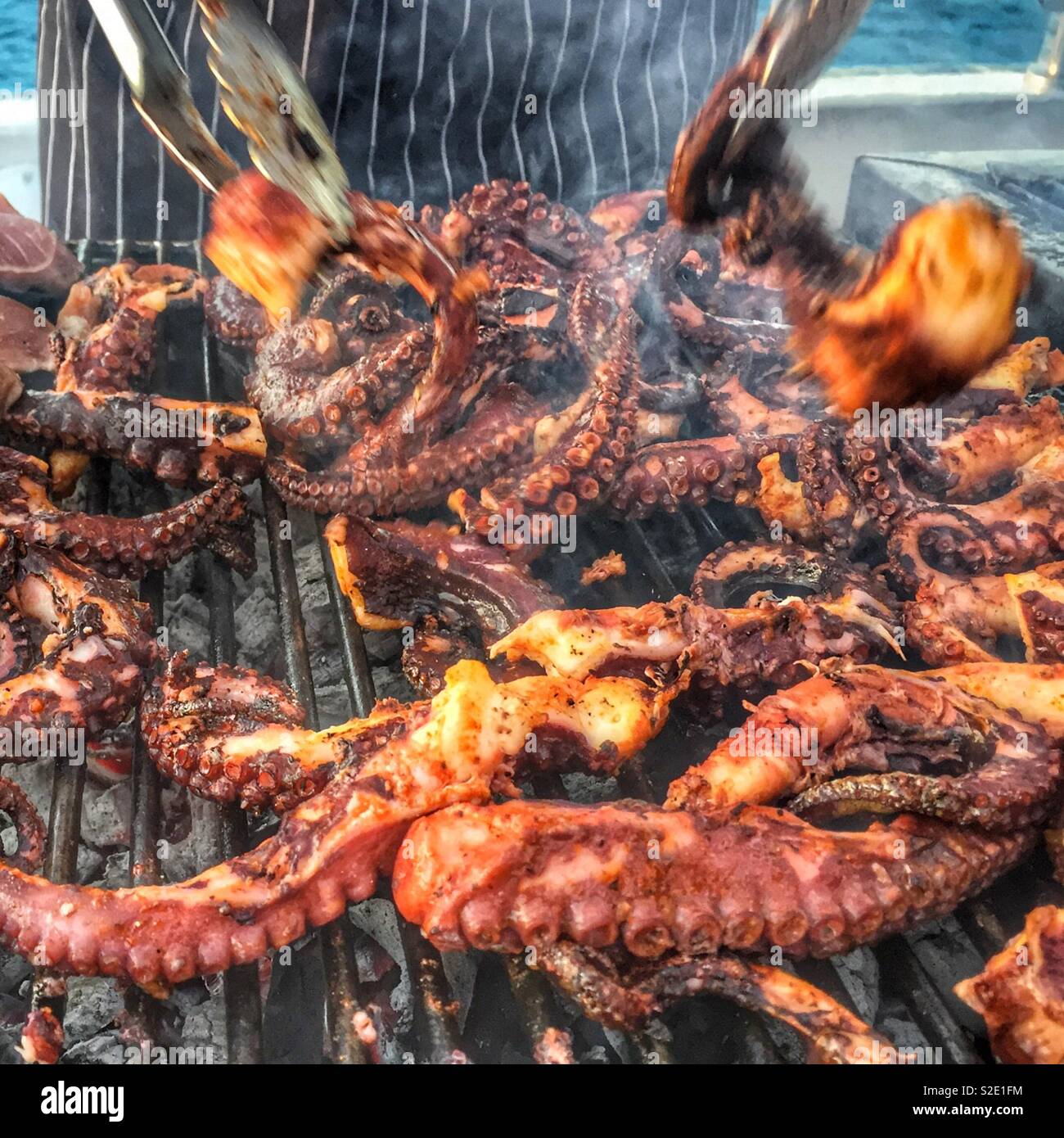 Chef tosses Octopus tentacles while cooking on outdoor grill or bbq. Person cooks octopus, seafood on bbq. Stock Photo