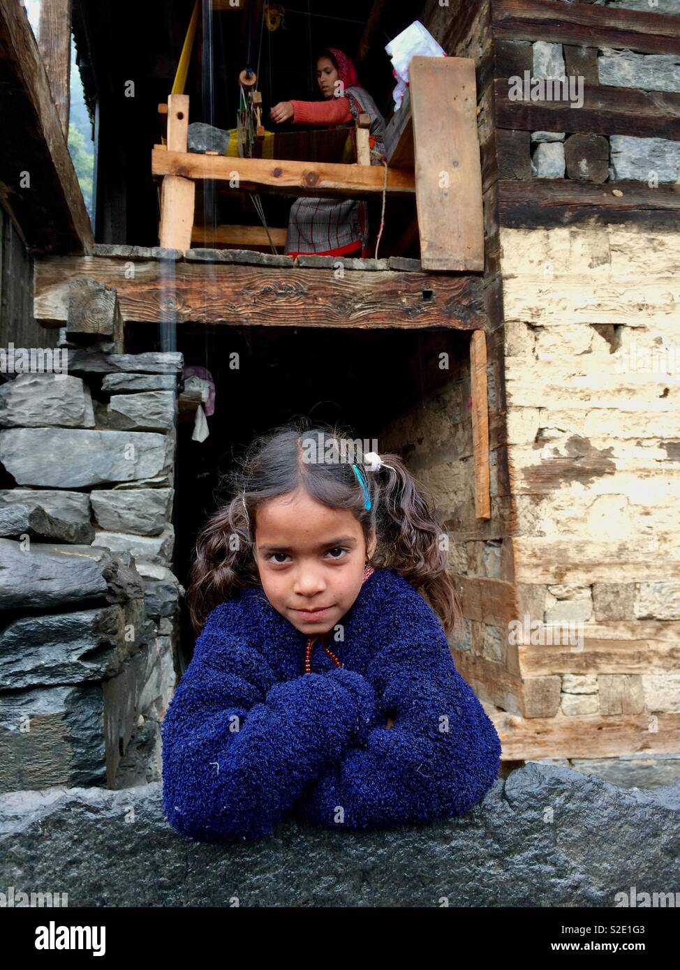 Curious kid outside the courtyard and in the background her mother weaving a shawl. Stock Photo