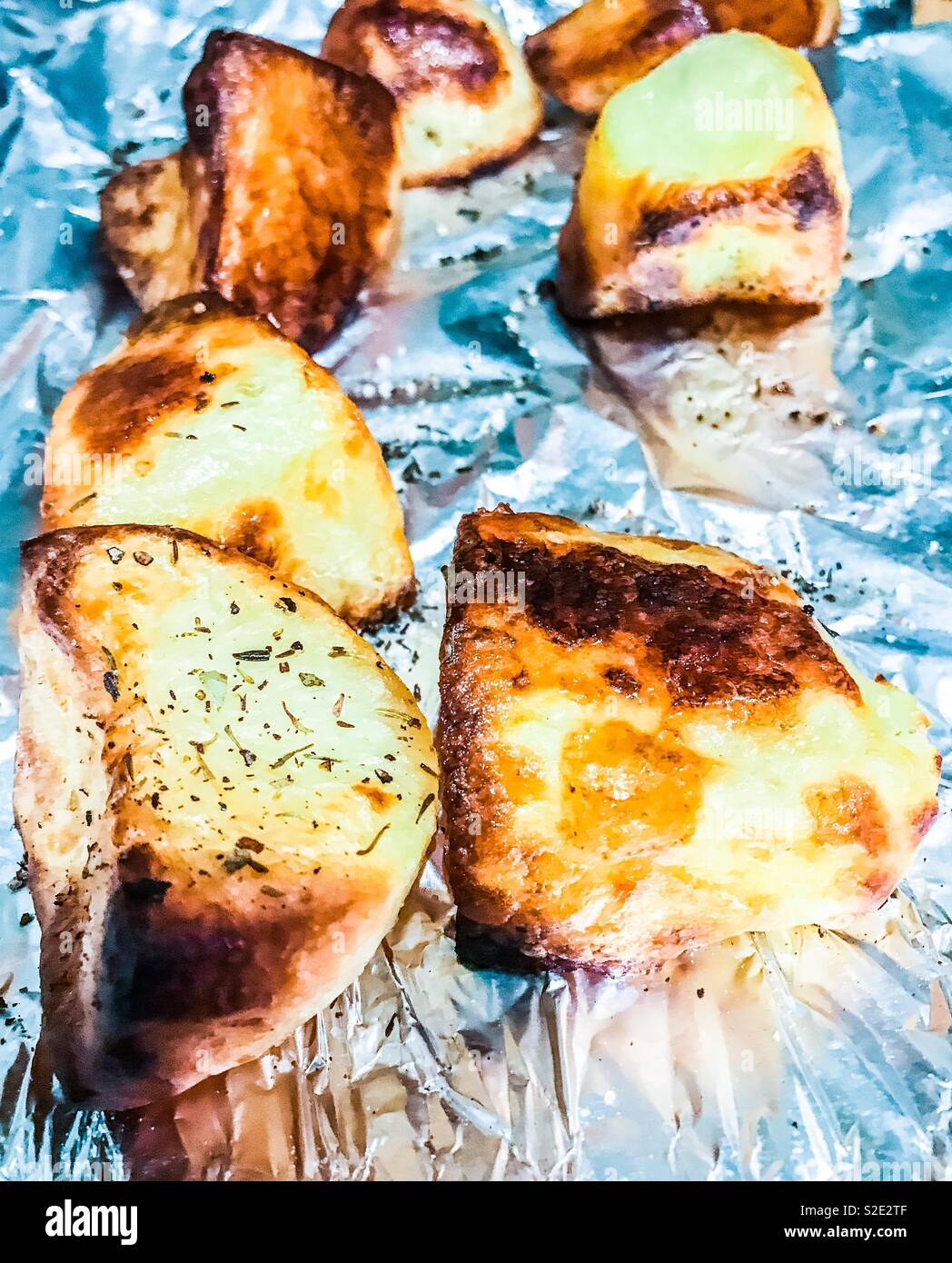 Roast potatoes cooked with seasoning on silver foil Stock Photo