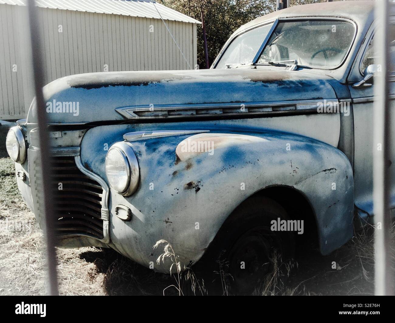 Old, rusty, gray Chevrolet coupe parked behind metal fence - Smartphone Captured Stock Image