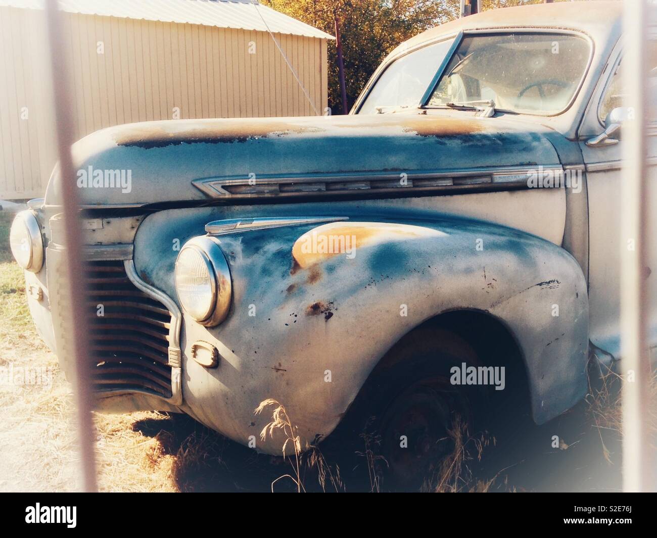 Vintage rusty, gray Chevrolet coupe parked behind metal fence - Smartphone Captured Stock Image
