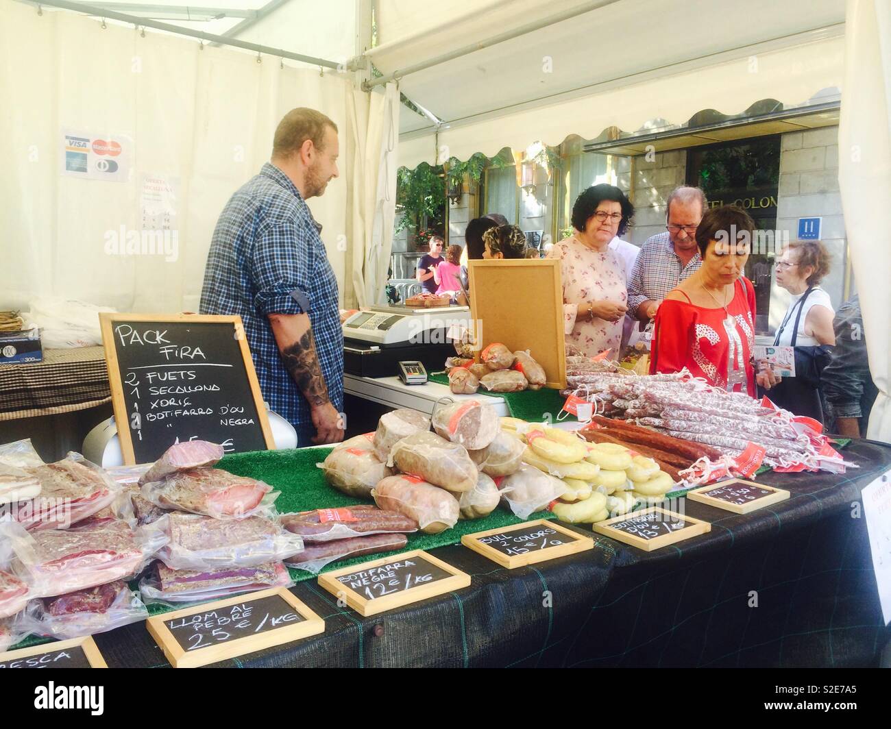 Food stall selling sausages and salamis at busy food market in central Barcelona in Spain - Smartphone Captured Stock Image