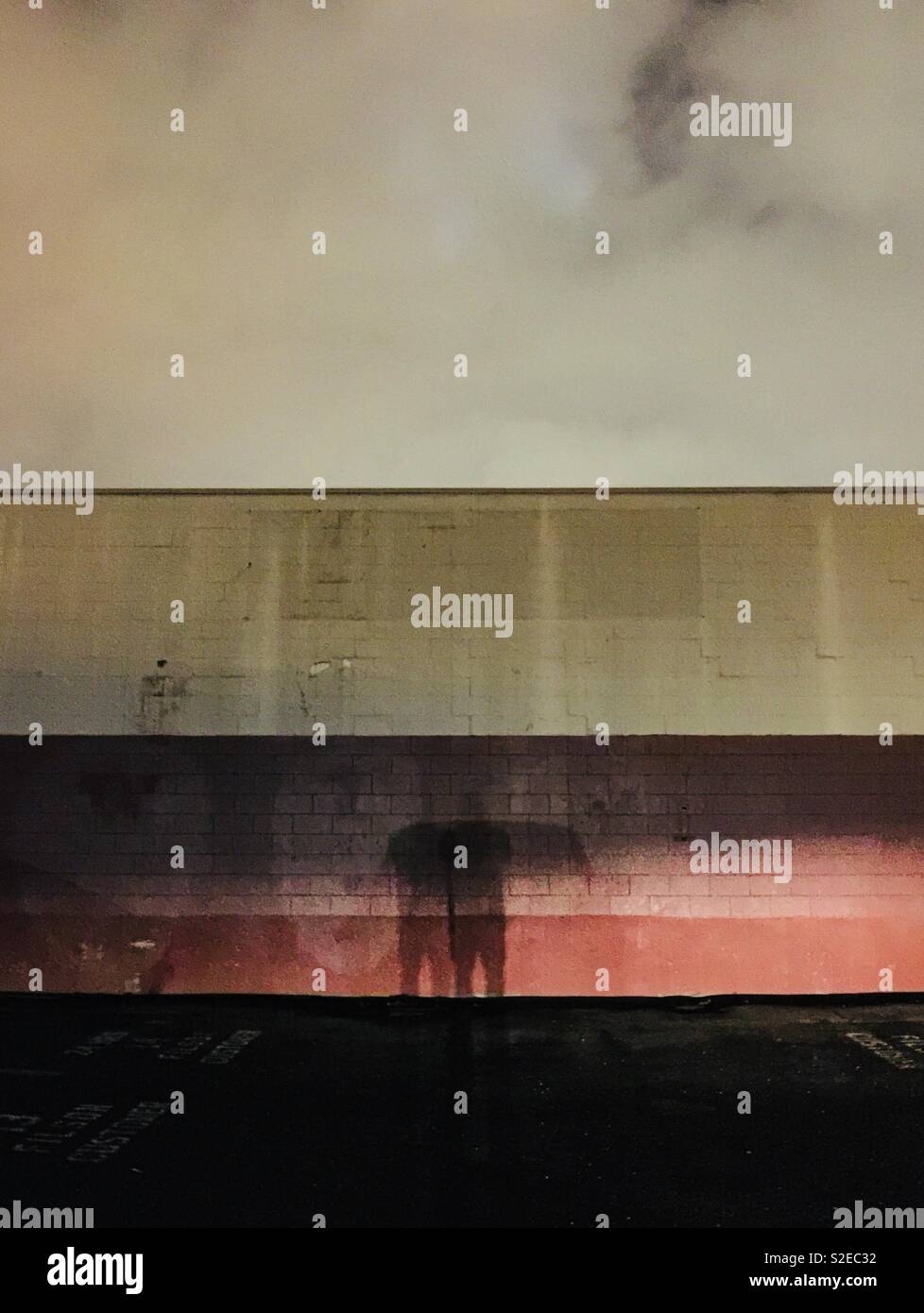 Mysterious shadow of a person at night against a painted urban wall - Smartphone Captured Stock Image