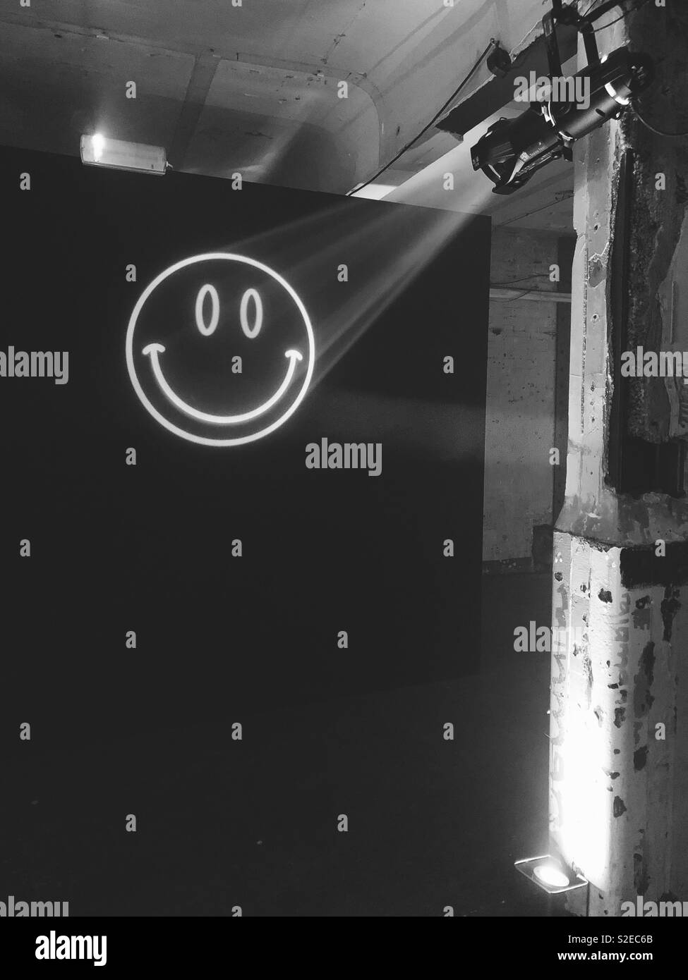 Rave style smiley face projection against black background at warehouse party in London, England. Black and white Stock Photo