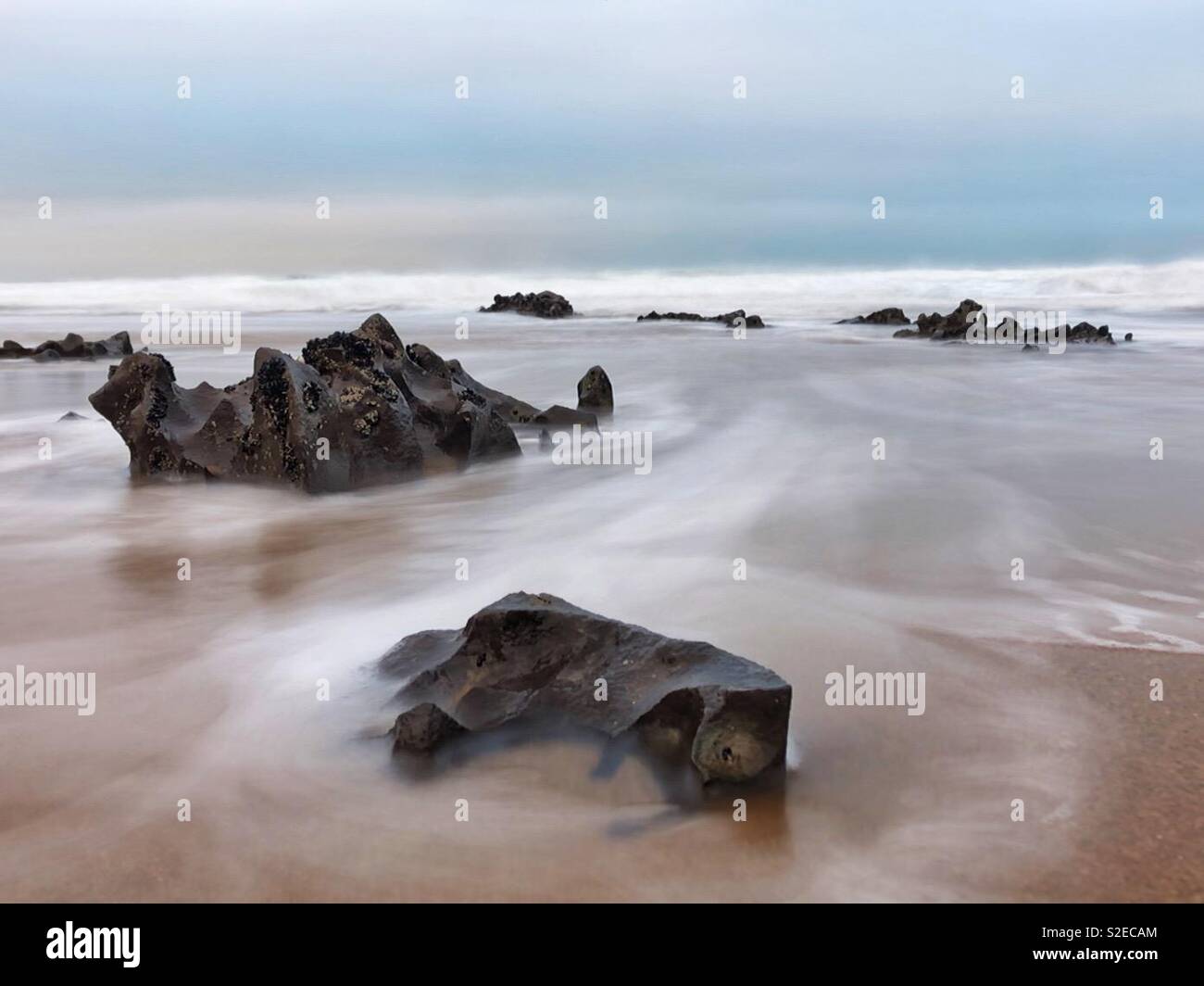 Incoming morning tide washing around rocks on a Welsh surf beach during rough weather, November. Stock Photo