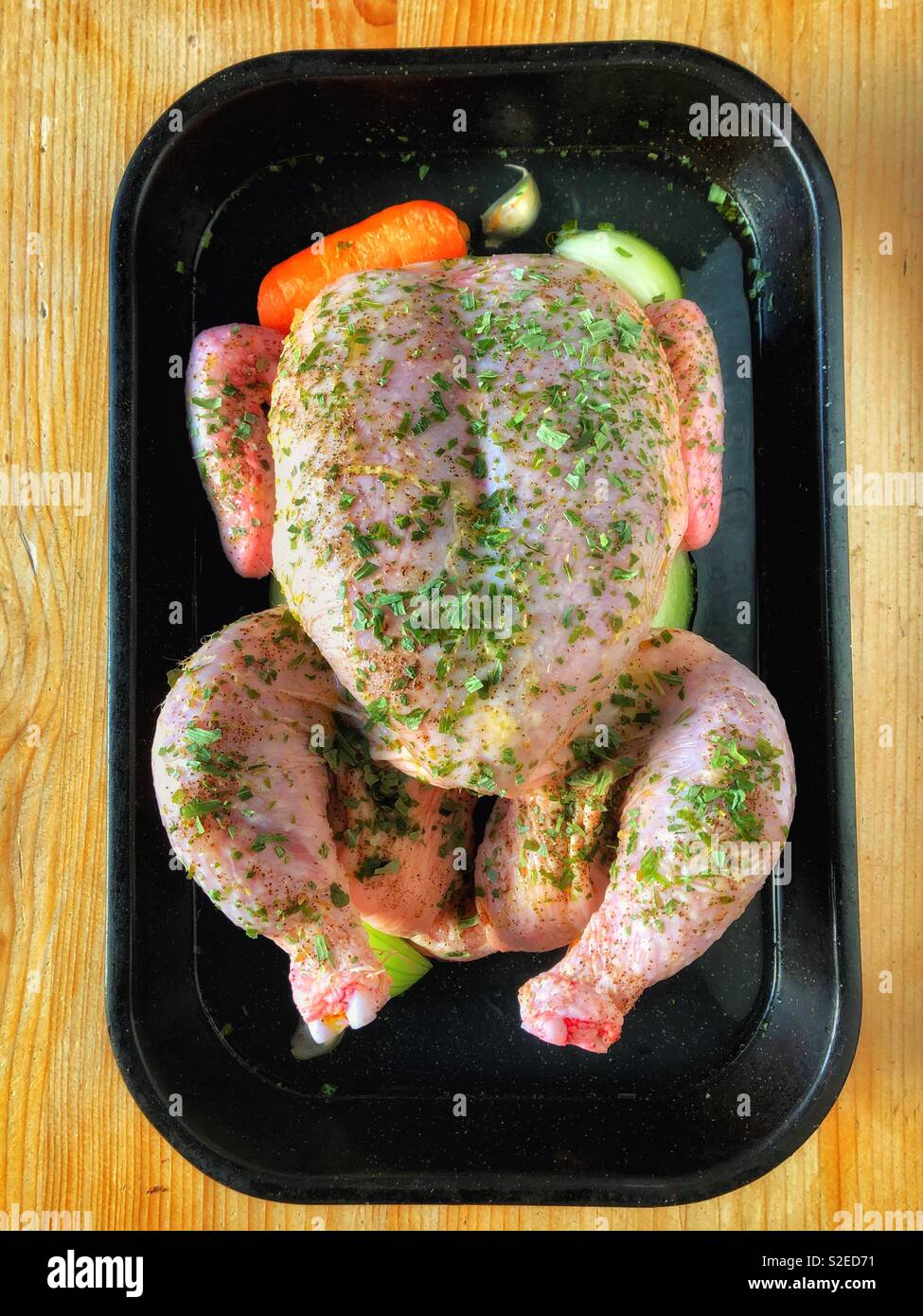 A chicken prepared for roasting in a roasting tin with root vegetables, sprinkled with Tarragon. Stock Photo