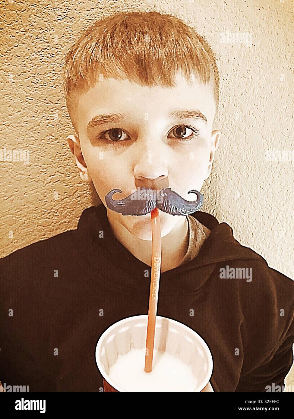 A young boy drinking milk with a funny mustache straw. Funny kids. Stock Photo