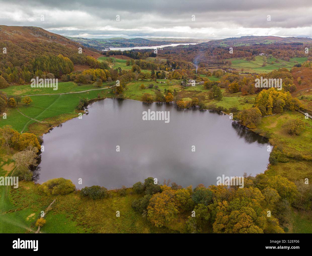 Aerial shot of Loughrigg tarn in Cumbria with smoke rising from a house in autumn - Smartphone Captured Stock Image