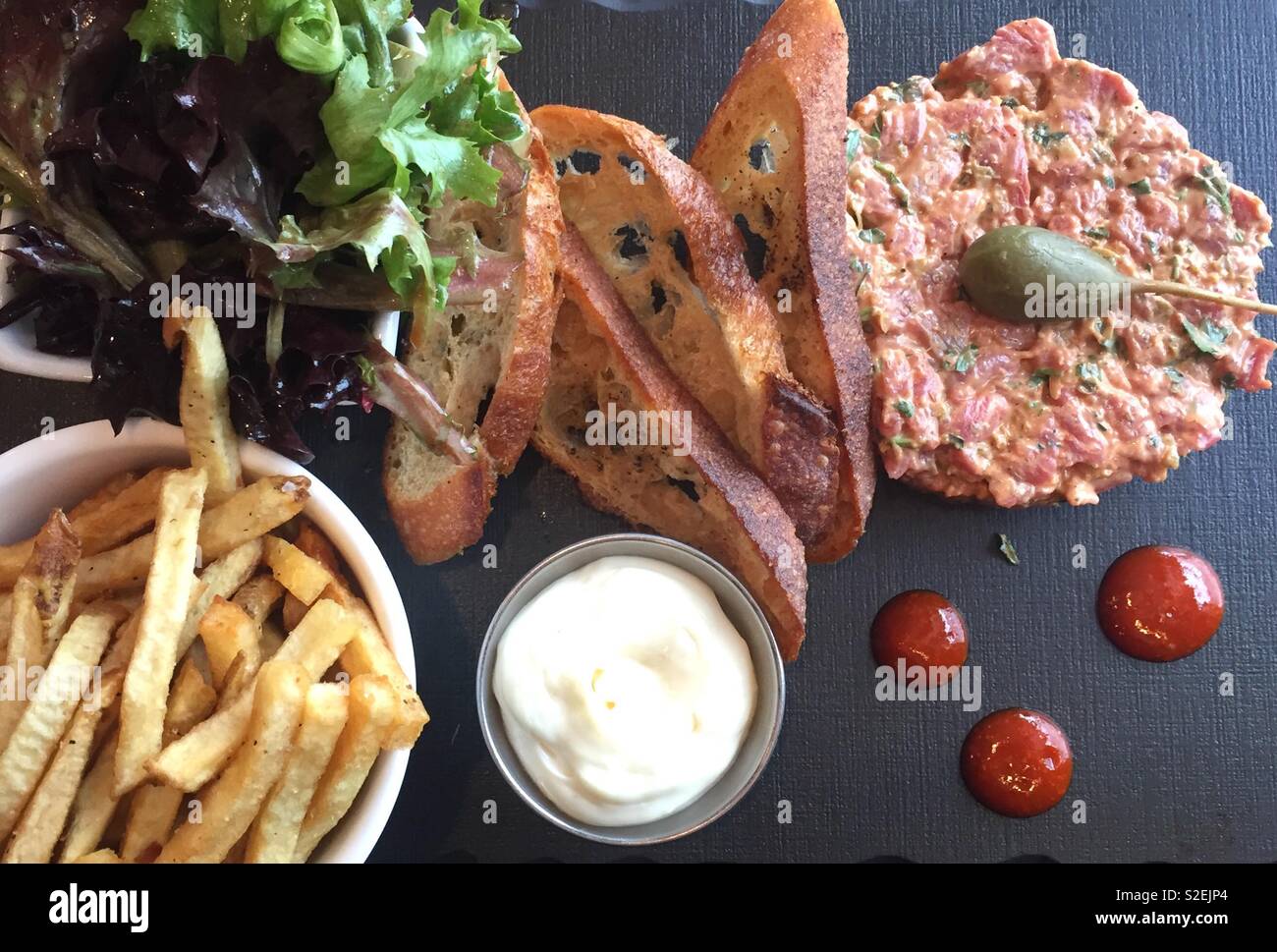 Restaurant meal with beef tartar, french fries, mayonnaise sauce and green salad. Big caper on the meat. - Smartphone Captured Stock Image