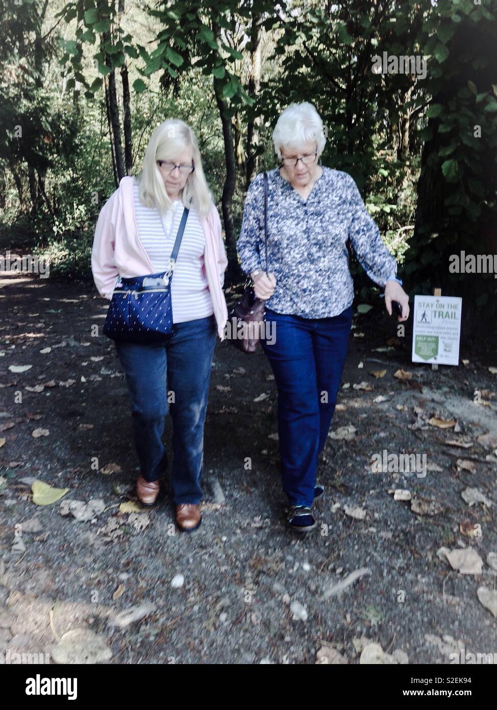 Deep in conversation, two middle aged sisters walk through Seattle park - Smartphone Captured Stock Image