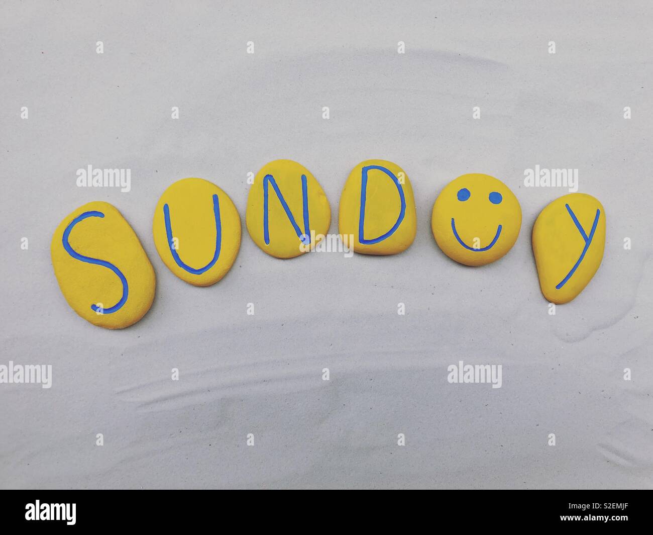 Sunday word with yellow painted stones over white sand - Smartphone Captured Stock Image