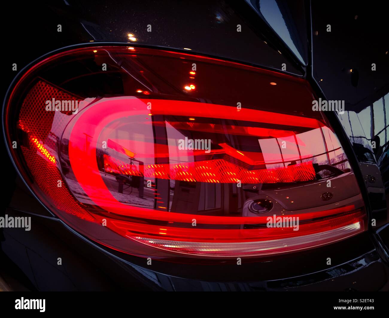 Stylish tail light of an automobile on show reflects the new car showroom in shimmering shades of red. Concepts: interior, elegance, reflection, modernism. Design elegance. Automotive. Stock Photo