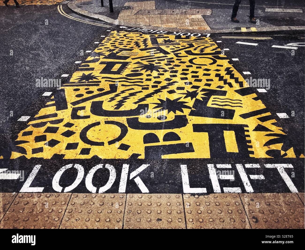 Bright yellow paint is used on a road junction to alert pedestrians as to which way they should be watching in order to be street safe. - Smartphone Captured Stock Image