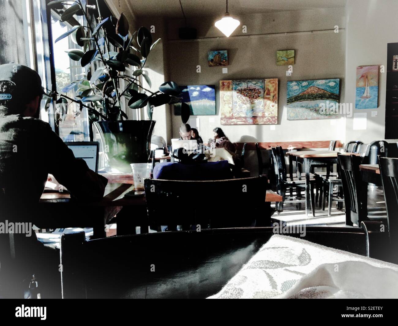 Muted morning photo of Seattle coffeeshop and customers absorbed in their electronic devices, with artwork on the walls - Smartphone Captured Stock Image