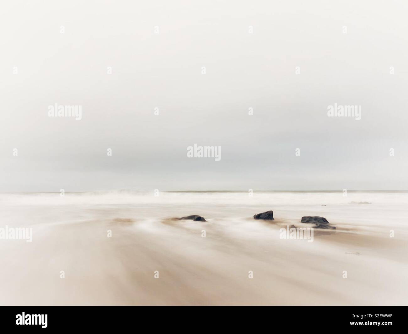 High key image of water washing over rocks on a remote Welsh beach, November. - Smartphone Captured Stock Image