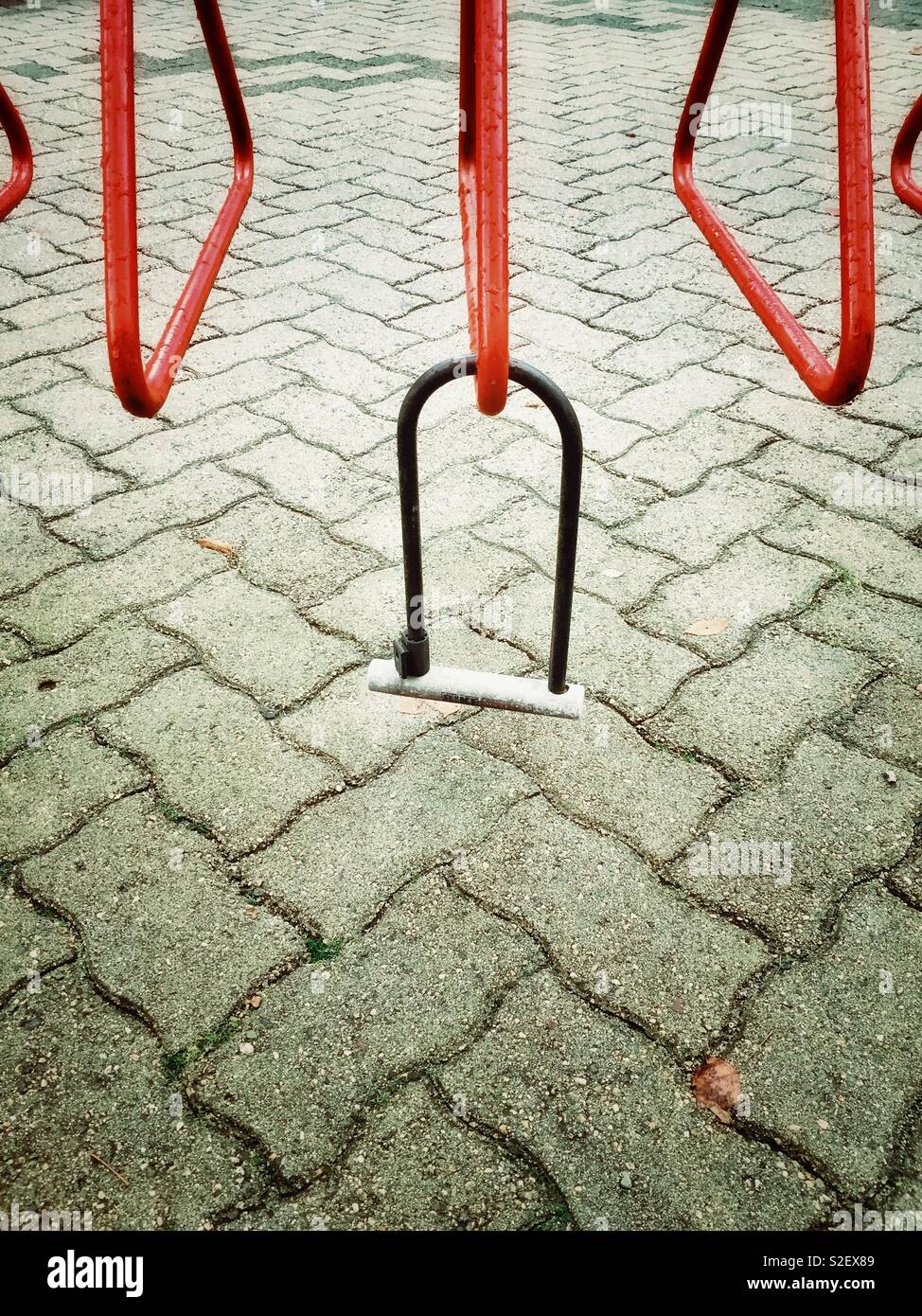 Dangling metal bicycle lock left behind from missing stolen bike on an empty red cycle rack. Stock Photo
