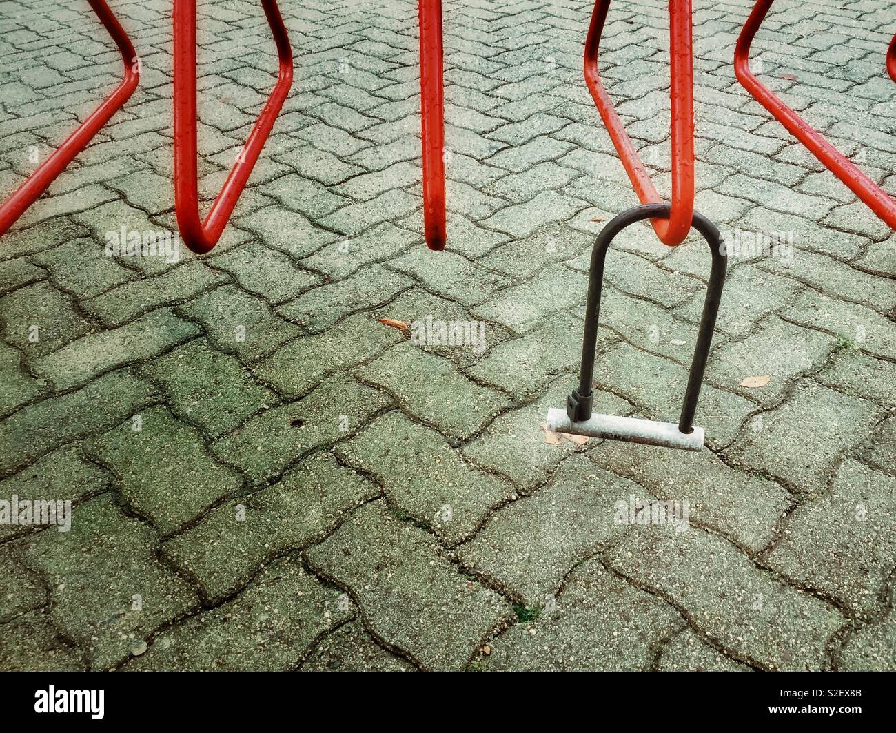 Metal bicycle lock left behind from missing stolen bike on an empty red cycle rack. Stock Photo