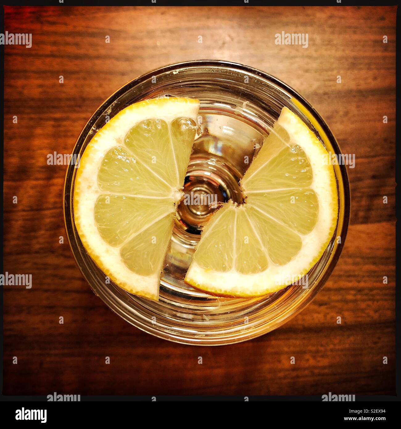 Looking down at a gin and tonic with ice and lemon on a wooden surface, a relaxing drink, warm colour scheme. - Smartphone Captured Stock Image