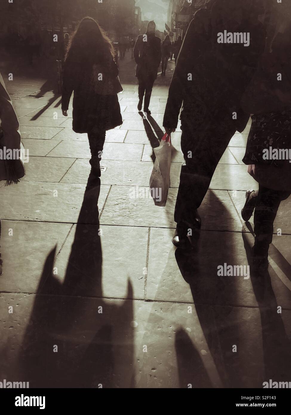 People walking in Buchanan Street, Glasgow, Scotland in strong sunlight, with long shadows, sepia image.  Silhouettes and carrier bags. - Smartphone Captured Stock Image