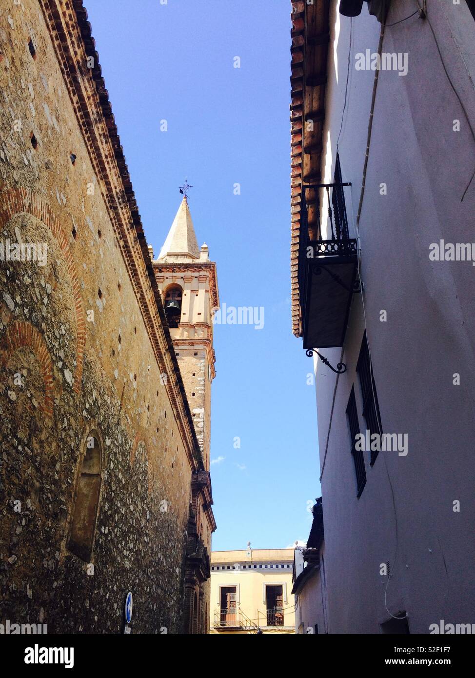 Between two high walls in a narrow alley a church steeple peeps through Alájar in Andalucia Spain Stock Photo