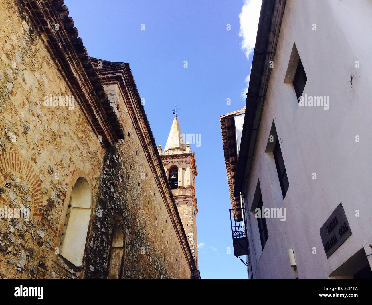 Looking up between two high walls in an alleyway a church steeple peeps through in a village in Andalucia Spain Stock Photo