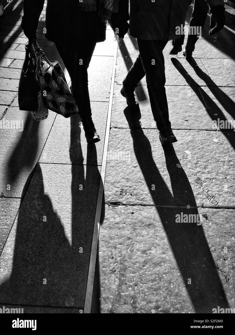 Monochrome/black and white image of people walking along Buchanan Street, Glasgow city centre, Scotland.  Strong sunshine, figures backlit. - Smartphone Captured Stock Image
