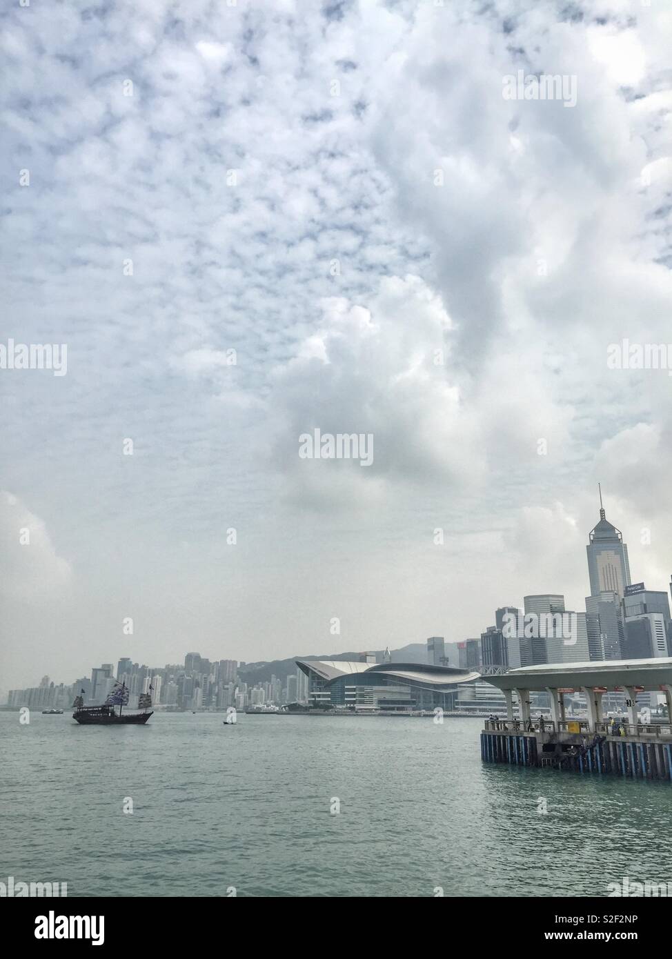 Aqua Luna II, a replica Chinese junk used for sightseeing cruises on Victoria Harbour, the HKCEC and the high rise commercial buildings of Wan Chai, Hong Kong Island - Smartphone Captured Stock Image