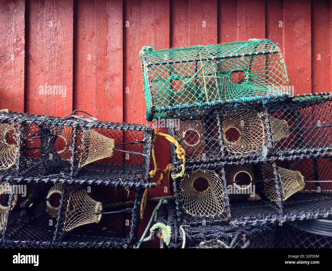 Empty crab pots or traps stacked up outside a red painted wooden shed in Valle, Norway. - Smartphone Captured Stock Image