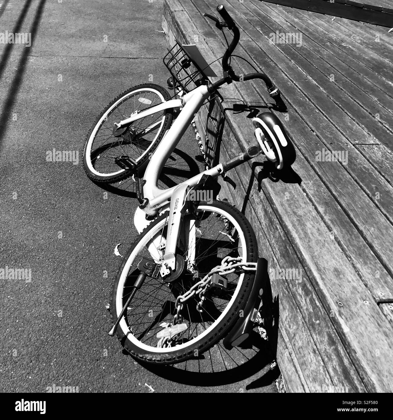 Rental bicycle leaning against a wooden raised area in black and white - Smartphone Captured Stock Image