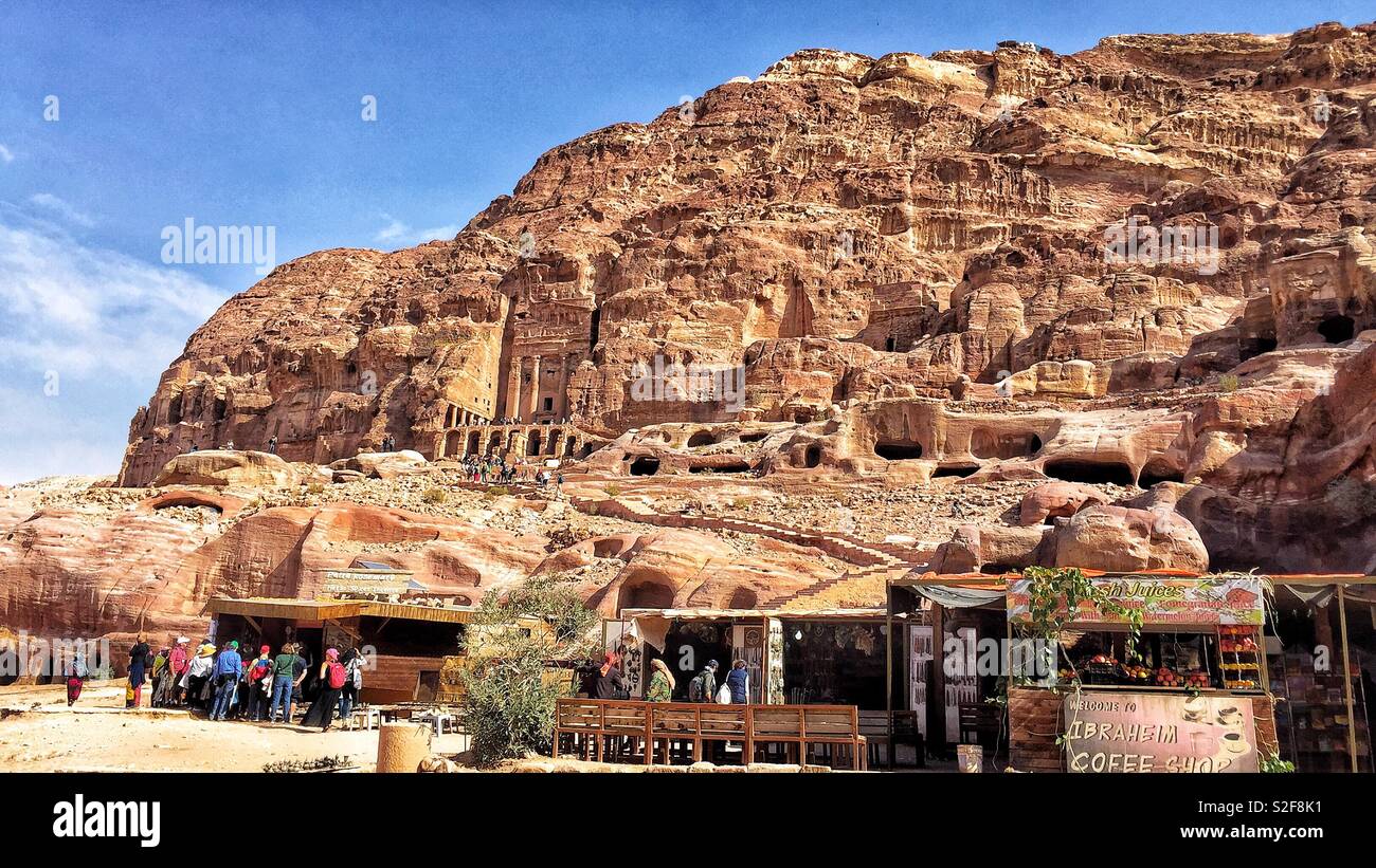 Photo of the little Shops and Cafe in Petra providing refreshments for the Tourists. Above are The Tombs carved out of rock by the Ancient Nabataeans in the Rose Red City of Petra, Aqaba, Jordan. Stock Photo