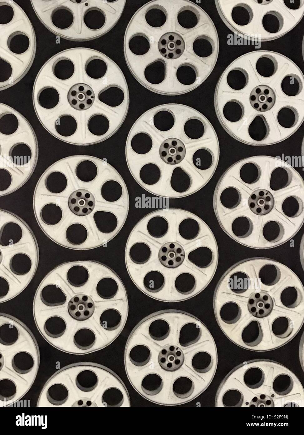 Many vintage, metal film reels are shown arranged on display, set against a black background. - Smartphone Captured Stock Image