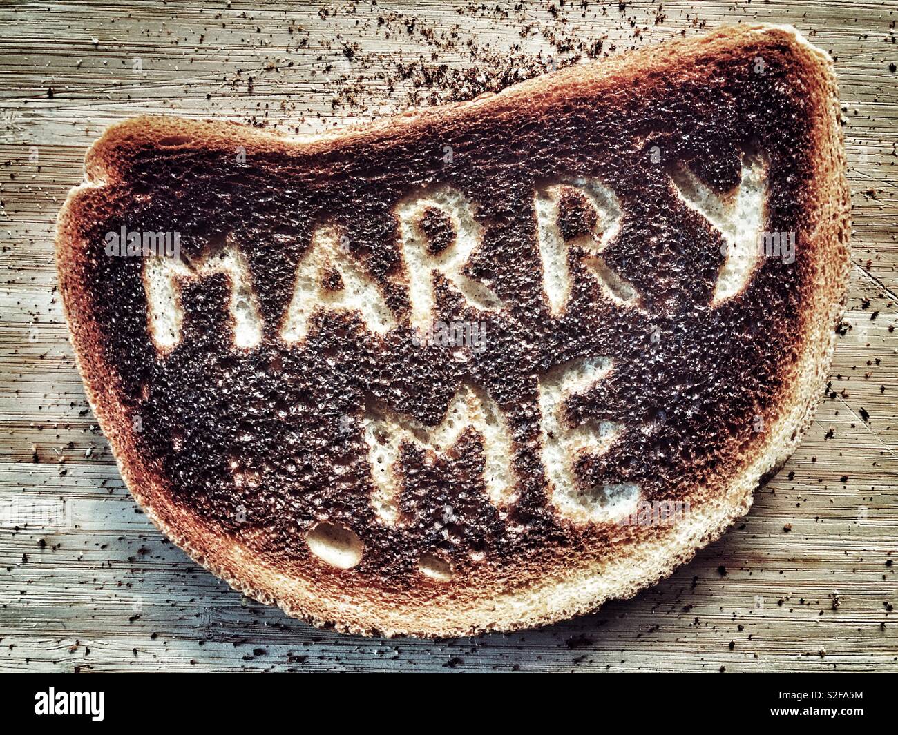 Creative food photography. Burnt toast with the words Marry Me scraped on to the charred surface - Smartphone Captured Stock Image