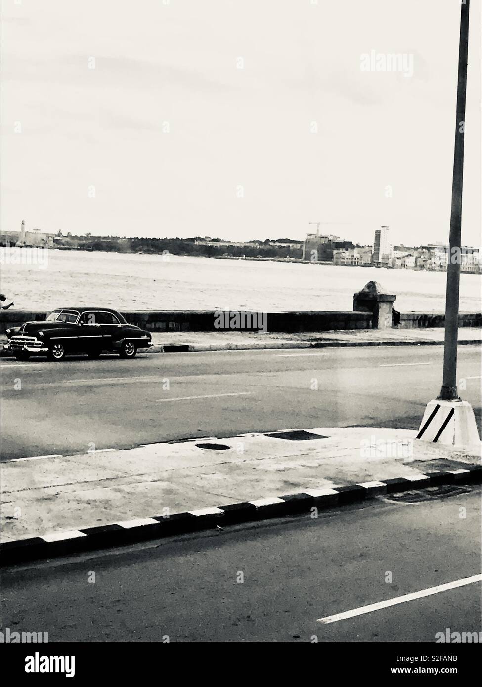 Black and white photo of the Caribbean Sea with a classic car parked up. Stock Photo