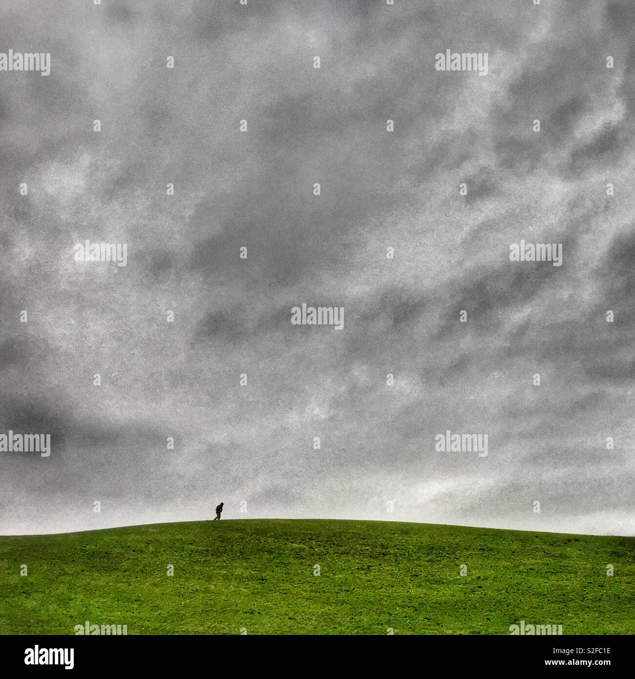 Lone walker on green hill against a grey dramatic sky - Smartphone Captured Stock Image