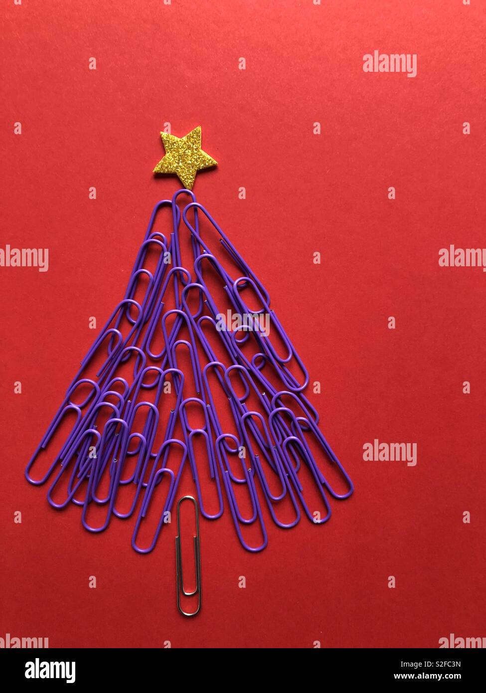 Creative Christmas concept. Christmas tree made from purple paper clips topped with a gold star on a red background with copy space - Smartphone Captured Stock Image