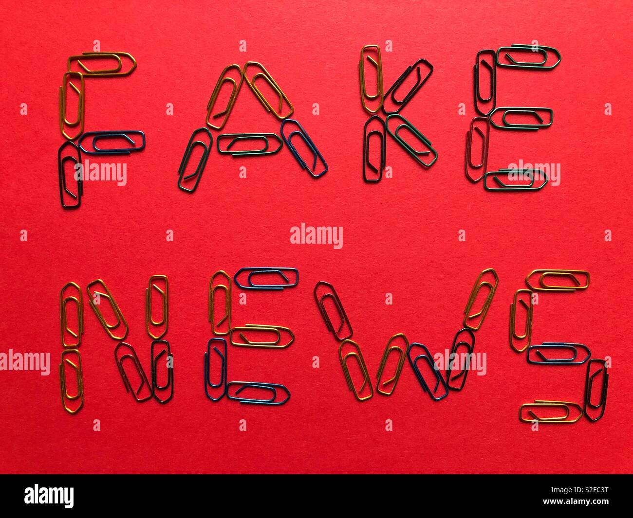 Fake News written in paper clips on a red background - Smartphone Captured Stock Image