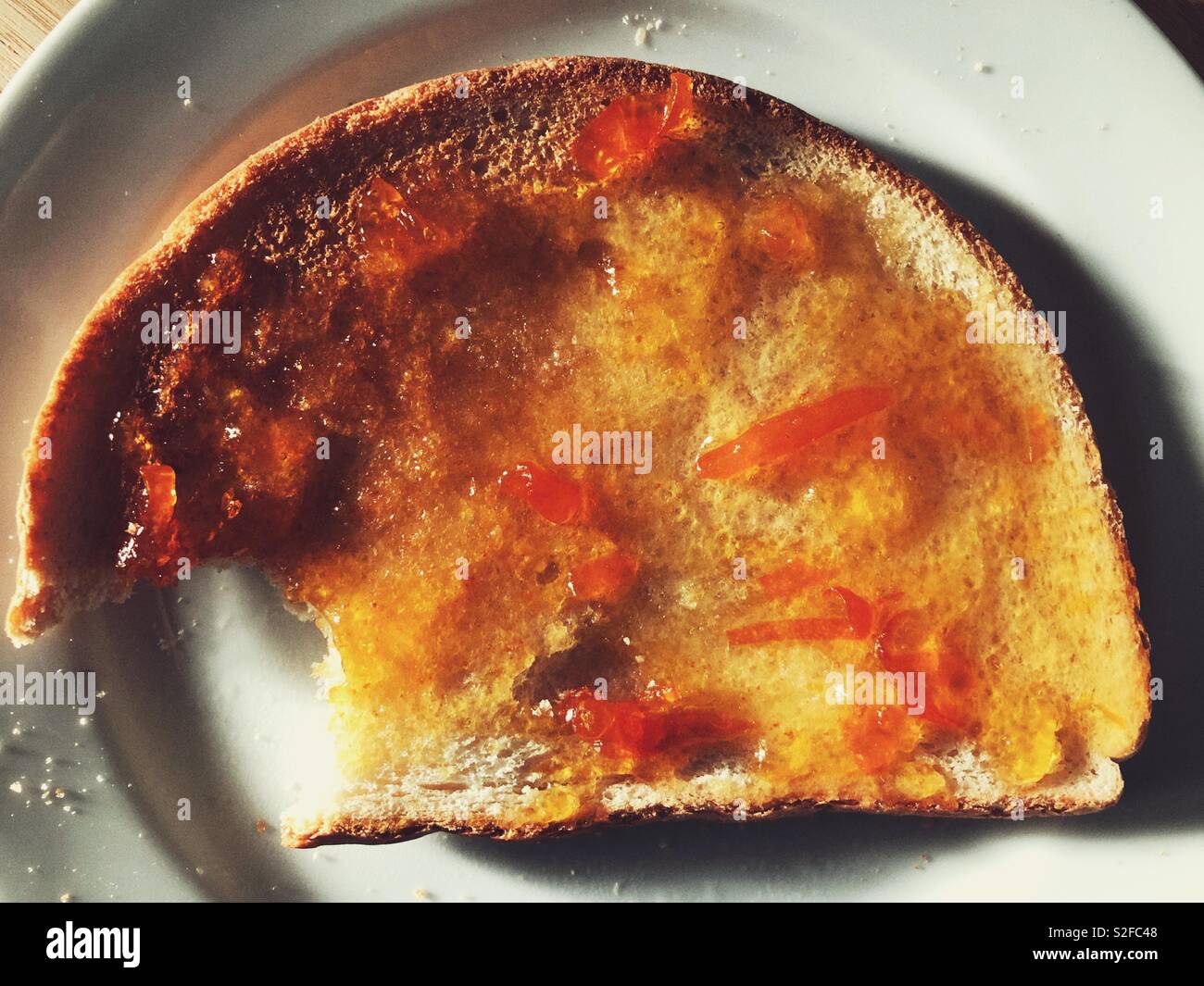 Toast and marmalade with a bite missing, on a white plate - Smartphone Captured Stock Image