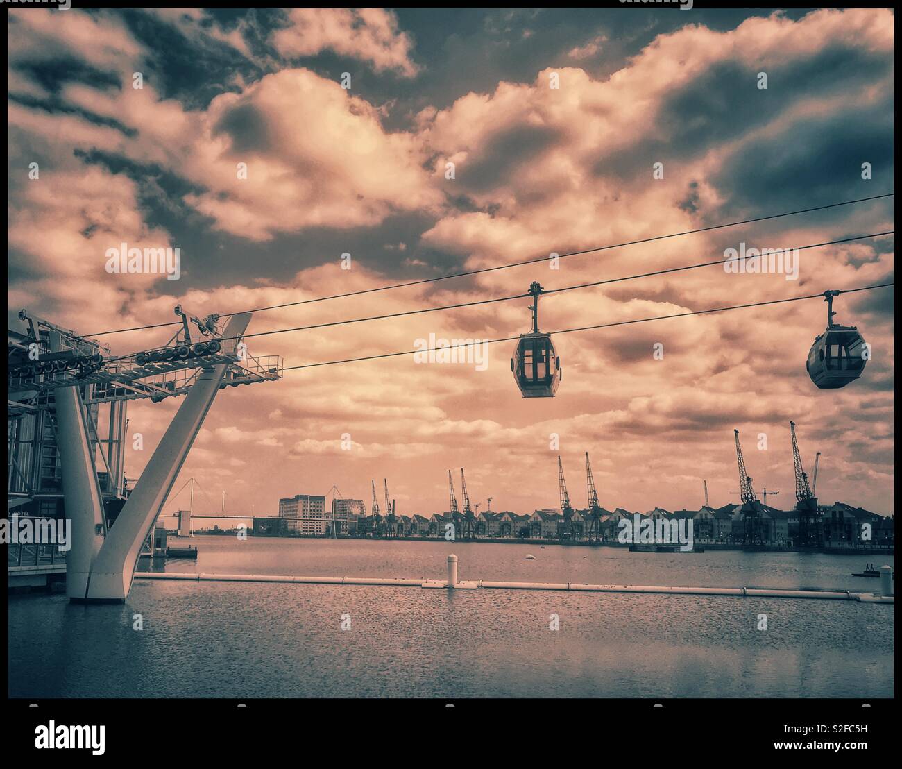 Two cable car pods of the Emirates Air Line Cable Car transport system depart & arrive at the Royal Victoria Docks terminal. This iconic transport system traverses the River Thames in London, England. - Smartphone Captured Stock Image