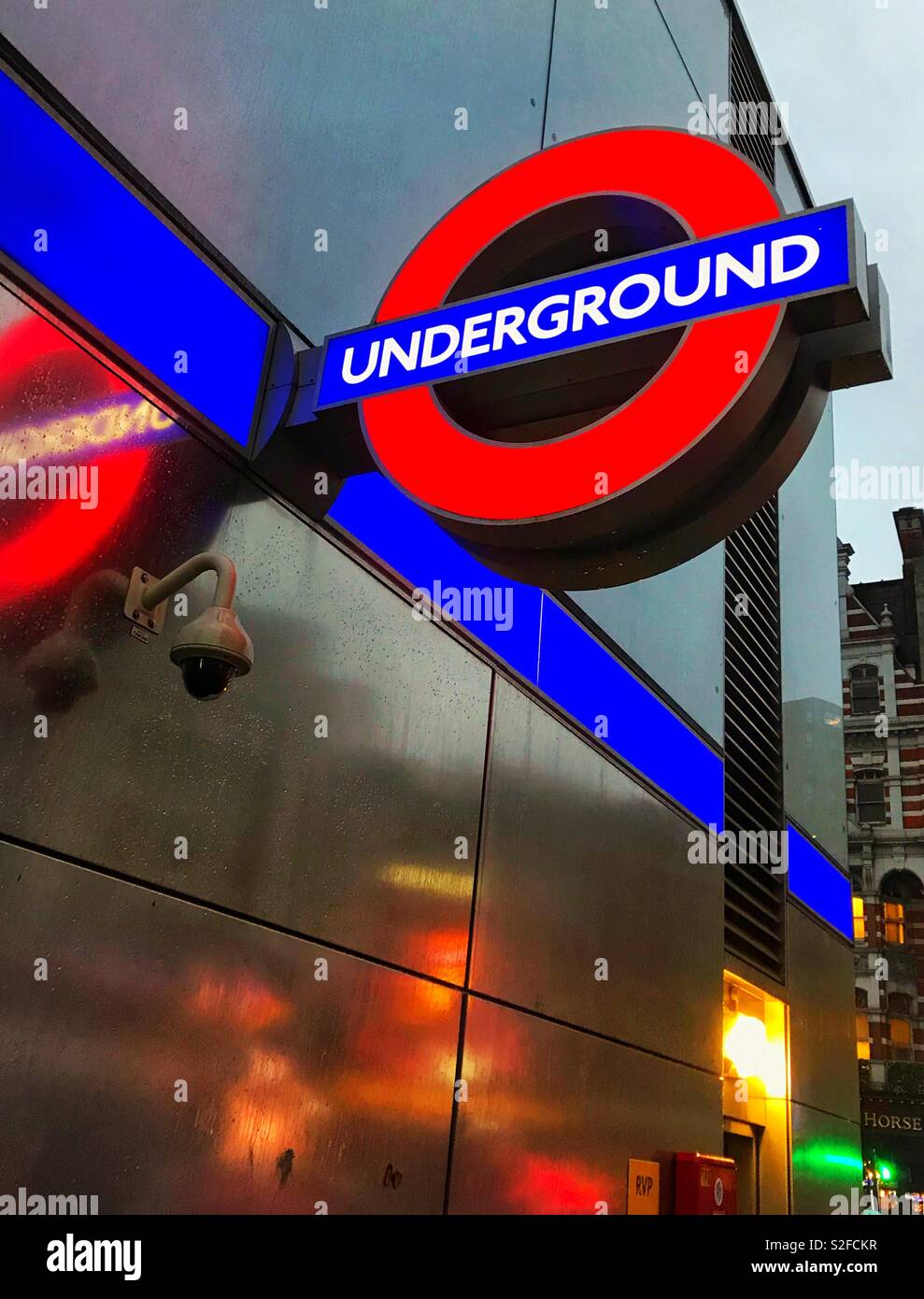 Sign outside a London Underground station on a dark, wet, winter’s afternoon with lights reflected on the wall Stock Photo