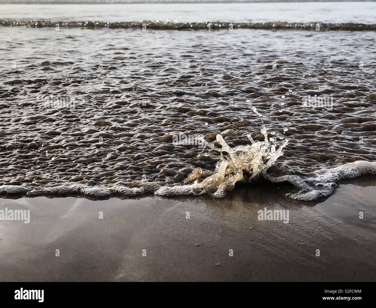 Incoming tide splashing against a pebble on the beach - Smartphone Captured Stock Image