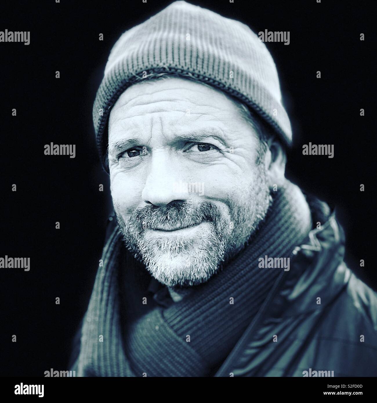 Head and shoulders portrait in monochrome of a middle aged man in a beanie hat wearing a hat and scarf. Stock Photo