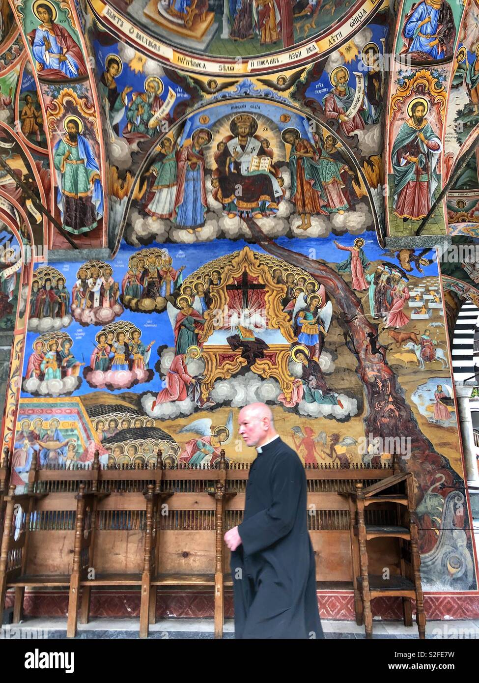 A priest walking by the colourful painted walls of the Rila Monastery, a UNESCO World Heritage Site in Bulgaria. - Smartphone Captured Stock Image