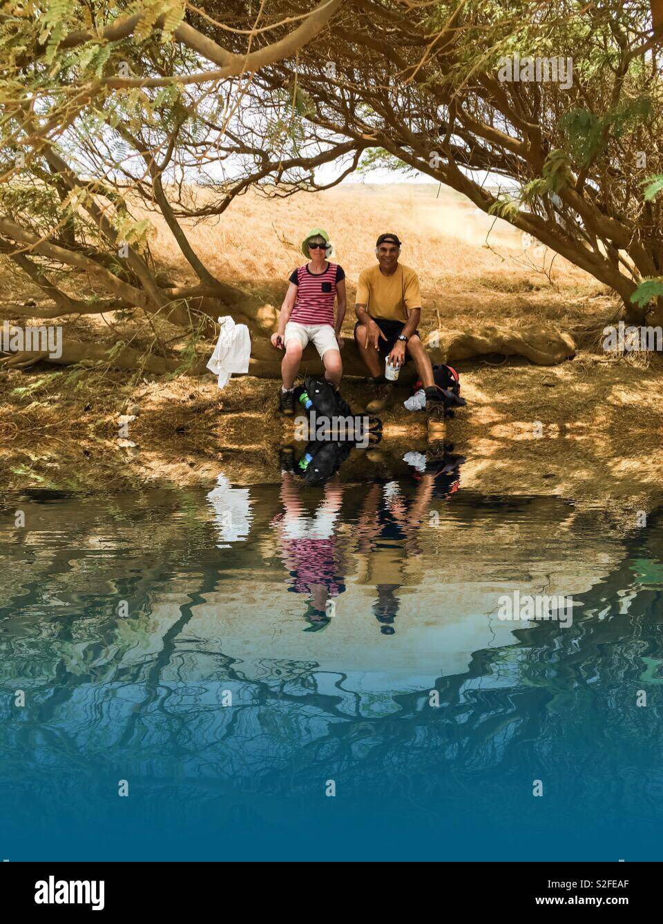 Sitting pretty. A man and a woman reflected in a puddle. Taking a break from a hike. - Smartphone Captured Stock Image