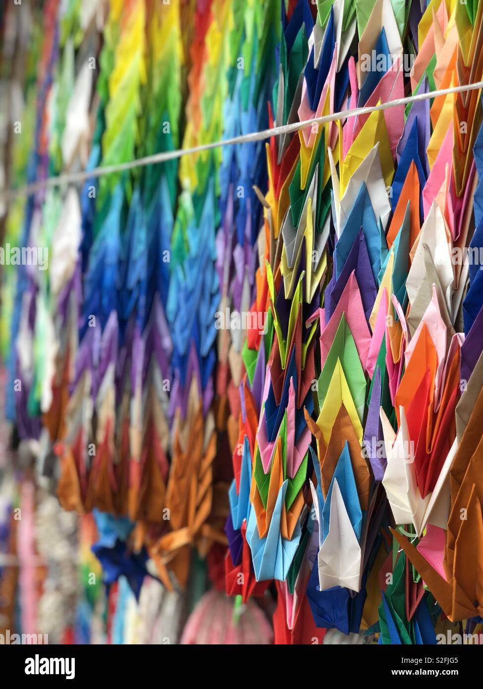 An offering of 100 folded paper cranes on a string in a japanese shrine ...