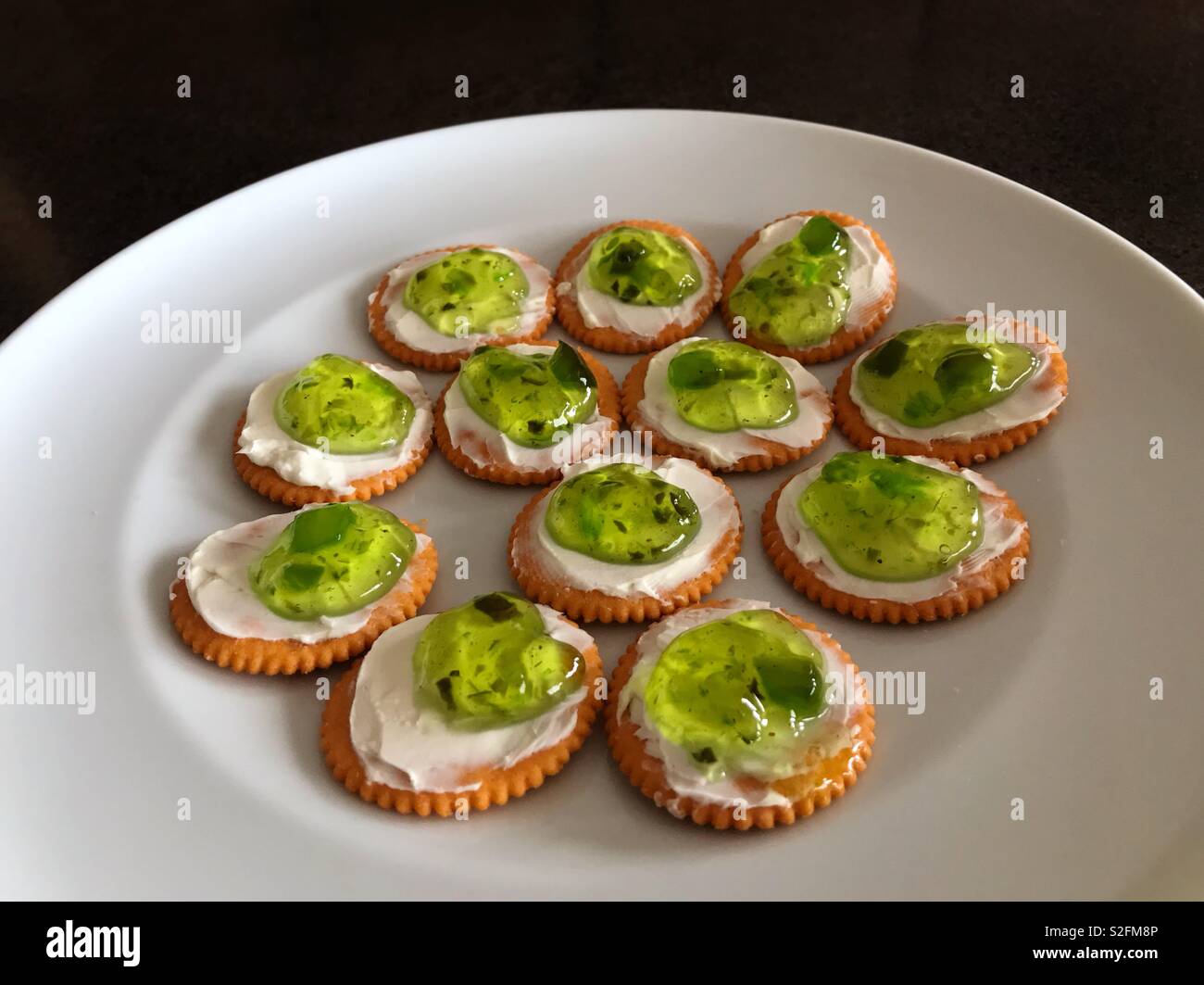 A savoury snack of crackers with cream cheese and jalapeño jelly on a